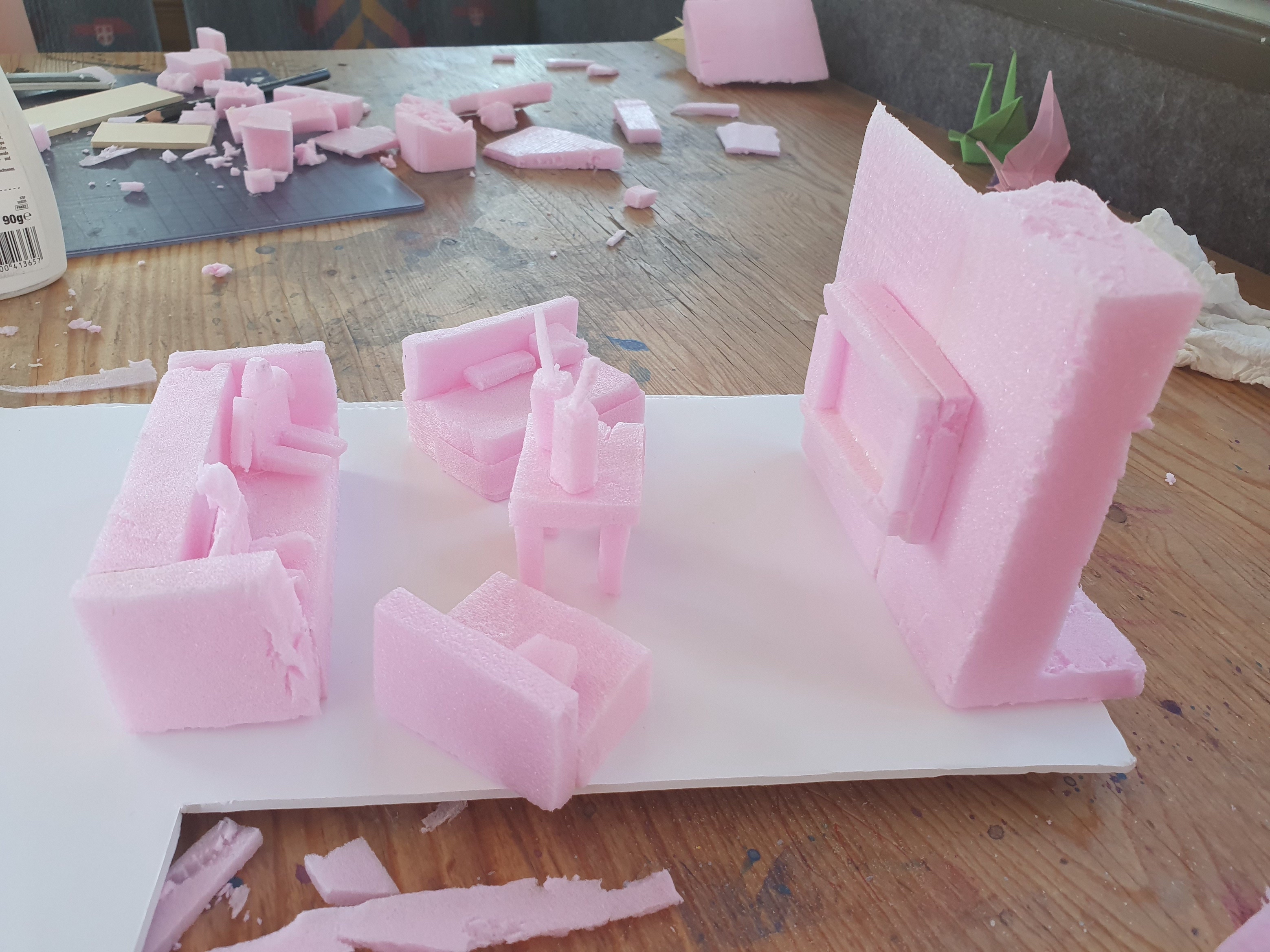 Foto eines pinken Styropor Modells. Darauf zu sehen ist eine Wohnzimmereinrichtung. Couches mit Menschen, ein kleiner Tisch mit Getränken, eine Wand mit Fernseher.