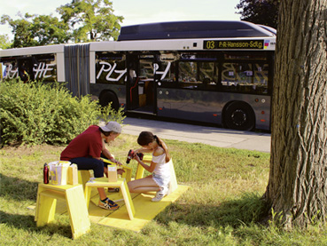 Das Bus-Labor - ein umgebauter ehemaliger Linienbus - an einem temporären Standort in der Wiener Per-Albin-Hansson-Siedlung und bastelnde Kinder auf einer Wiese