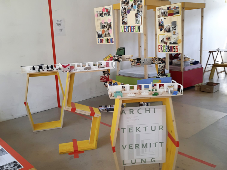 Ausstellungselemente aus gelben Doka-Platten mit Architekturmodellen und Plakaten