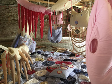 Raum mit Ziegelwänden und textilen liegenden und hängenden Objekten
